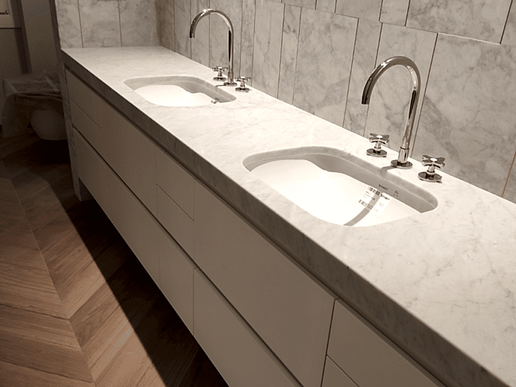 Bagno con pavimento in parquet Rovere modello spina ungherese. Piano lavabo e rivestimento parete in marmo Bianco di Carrara.